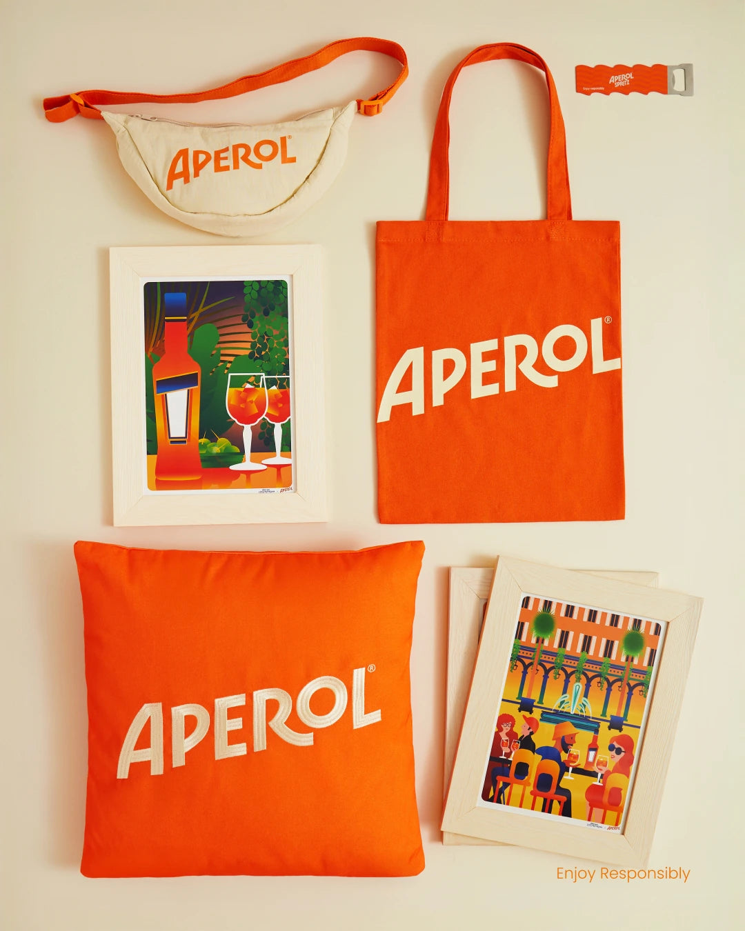 Orange Aperol products including a tote bag, pouch, and cushions on a light background